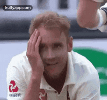 a man in a white shirt is smiling and covering his face with his hand .