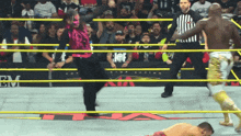 a wrestler in a pink mask stands in a ring with a referee behind him