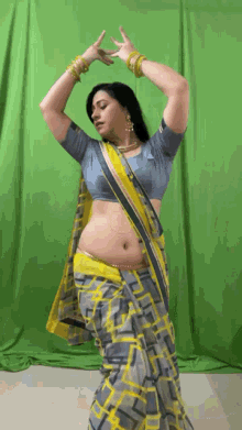 a woman in a yellow and grey saree is dancing in front of a green screen