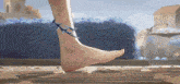 a woman 's foot with a bracelet on it is walking on a wooden floor .