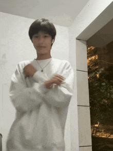 a young man wearing a white sweater and a necklace