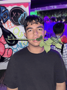 a man holds a rose in his mouth in front of a wall with graffiti on it that says xx