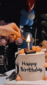 a person lighting a candle on a birthday cake that says happy birthday