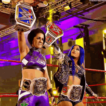two female wrestlers are holding up their championship belts in a ring