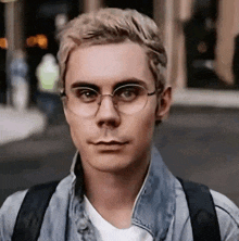 a young man wearing glasses and a denim jacket