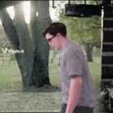 a man wearing glasses and a grey shirt is walking in a park with a viggle.ai logo in the corner