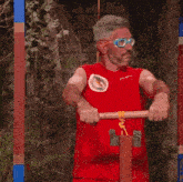 a man wearing glasses and a red givova shirt is standing in the mud
