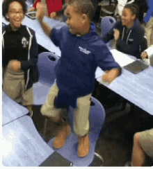 a boy in a blue shirt with the word eagle on it is jumping on a chair in a classroom