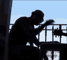 a silhouette of a man writing on a piece of paper on a balcony