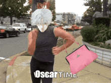 a man is running down a sidewalk with a pink purse that says oscar time on it