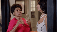 two women are standing next to each other in a doorway talking to each other .
