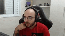 a bald man wearing glasses and headphones is sitting in a chair in front of a computer .