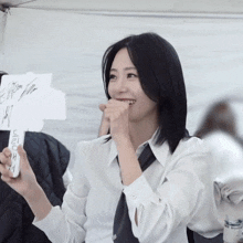 a woman wearing a white shirt and tie is holding a sign that says ' e ' on it