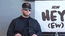 a man wearing sunglasses stands in front of a sign that says hey ( ew )