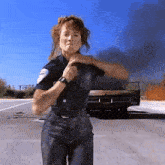 a woman in a police uniform is standing in front of a car that is on fire