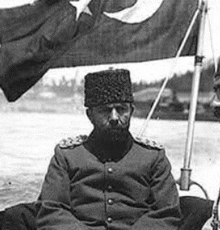 a black and white photo of a man in a military uniform sitting on a boat .