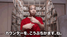 a bald man in a red shirt is standing in front of a bookshelf with chinese writing on it
