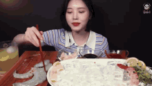 a woman is eating a plate of shrimp with chopsticks