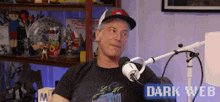 a man wearing a hat is sitting in front of a microphone with the words dark web above him