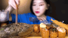 a woman in a blue shirt is eating a bowl of noodles with chopsticks