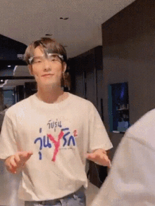a young man wearing a white t-shirt and glasses is standing in a room with his hands outstretched .