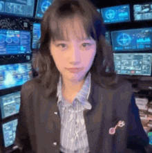 a woman in a suit is standing in front of a wall of monitors .