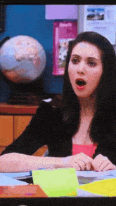 a woman is sitting at a desk with a globe in the background