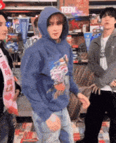 a boy in a blue hoodie is dancing in a room with other people