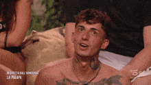 a shirtless man with a tattoo on his neck is sitting in front of a sign that says in diretta dall honduras la palapa