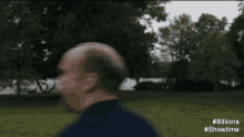 a man with a bald head is walking through a park .