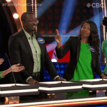 a man in a suit and a woman in a green dress are on a family feud game show