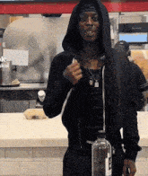 a man in a black hoodie holds a bottle of water in front of a sign that says ok skai