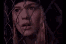 a woman is behind a chain link fence looking through it .