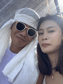 a man wearing sunglasses and a white towel around his head poses for a picture with a woman