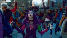 a woman with purple hair is standing in a crowd of people dancing on a street .