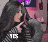 a woman in a striped shirt is pointing at her ear and the word yes is on the bottom