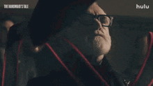 a man with glasses and a beard is holding a red ribbon in his hand .