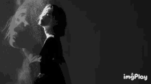 a black and white photo of a woman standing in front of a painting of a man .