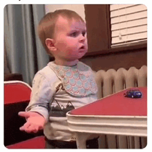 a baby is sitting at a table with his hands outstretched and a toy car on the table .