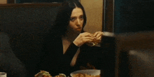 a woman in a black dress is sitting at a table eating a hamburger and french fries .