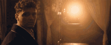 a man with curly hair is standing in front of a window