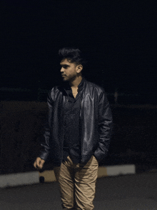 a young man wearing a black leather jacket stands in the dark