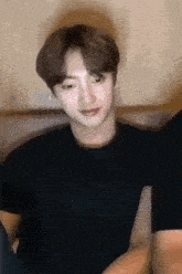 a young man in a black t-shirt is sitting on a couch and smiling .