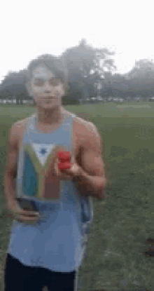a man in a tank top is holding a red object in his hand in a field .