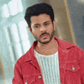 a man with a beard wears a red jacket and a white shirt