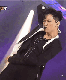 a man in a black suit is dancing in front of a spotlight with the word now on the bottom right