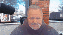 a man with a beard is sitting in front of a microphone with a picture of a man on the wall behind him