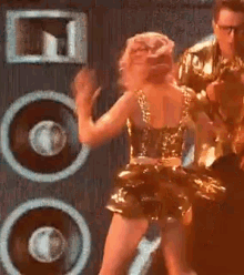 a woman in a gold dress is dancing on stage in front of a speaker .