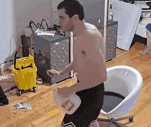 a shirtless man is holding a gallon of milk in a messy room