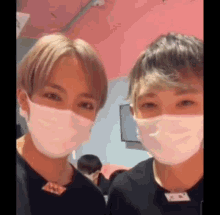 two young men wearing face masks are standing next to each other in front of a pink wall .
